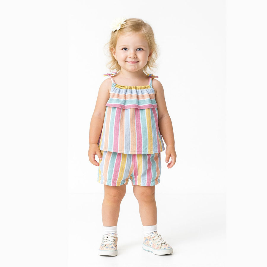 A young child smiling, wearing a matching top and shorts set with colorful vertical stripes, white socks, and patterned sneakers, standing against a plain white background.
