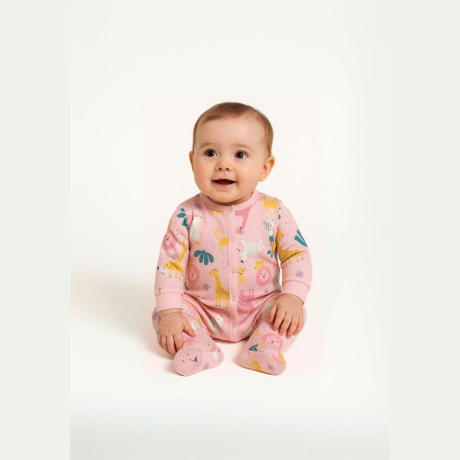 Baby wearing pink jungle animal print sleepsuit sitting on white background, showing front view with playful giraffe, lion and leaf designs