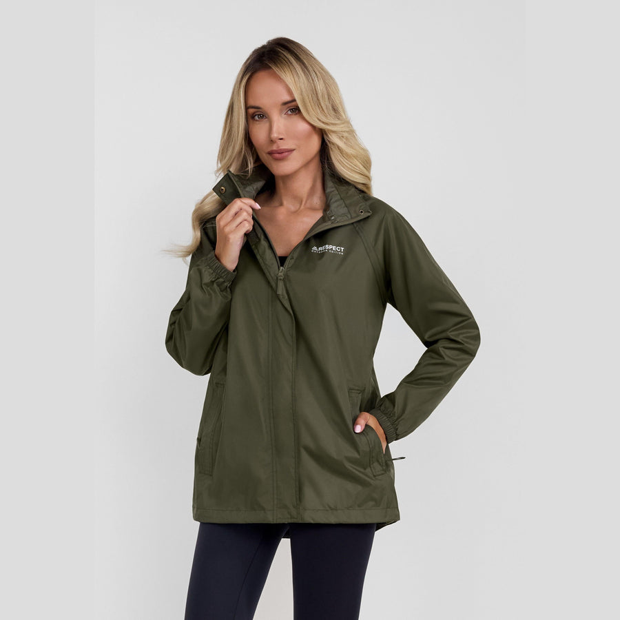 Woman wearing khaki waterproof jacket with hood up against white studio background, blonde hair, showing front view with protective zip closure