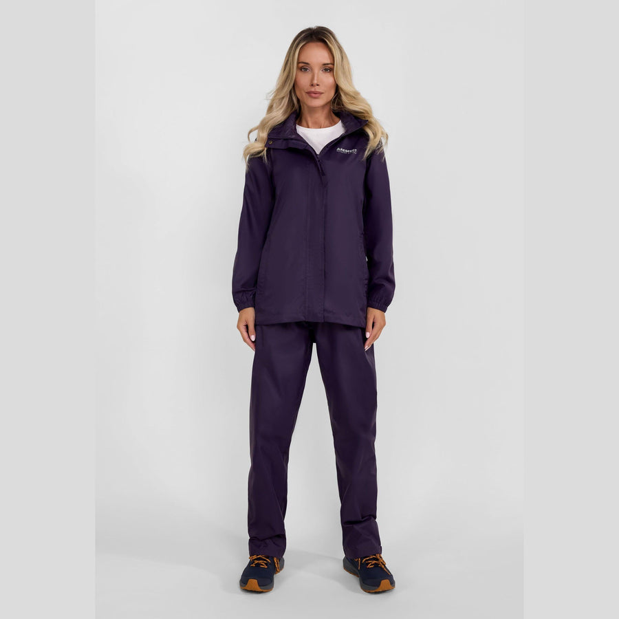 Woman wearing purple waterproof overpants and jacket set standing against white background, full body view showing complete rain protection outfit