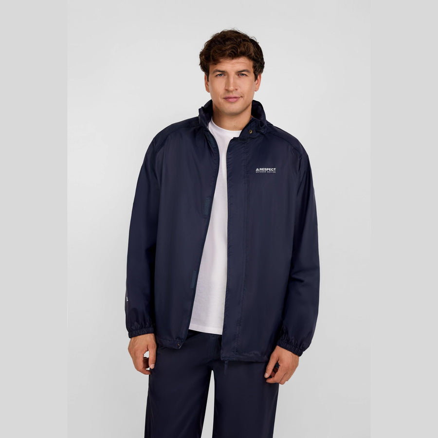 Young man wearing navy packaway waterproof jacket open over white t-shirt, standing against light background, showing regular fit and styling