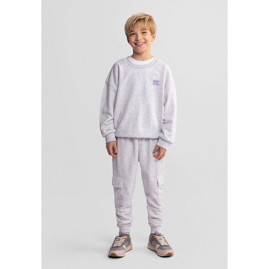Young boy wearing grey marl sweatshirt with matching joggers, smiling against white studio background