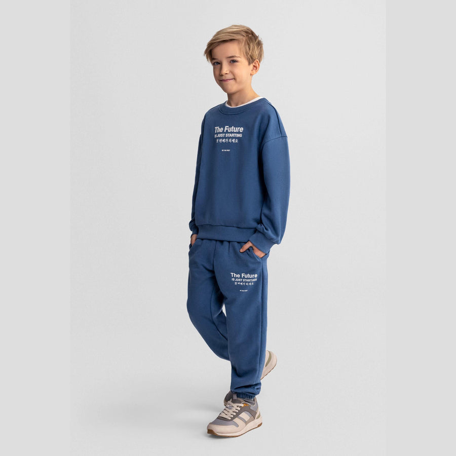 Boy wearing blue tracksuit set with 'The Future Is Just Starting' text graphics, posing against light grey background