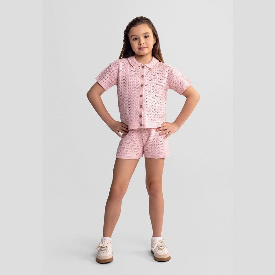 Young girl wearing blush pink pointelle knit set with button front cardigan and matching shorts, standing confidently against white background