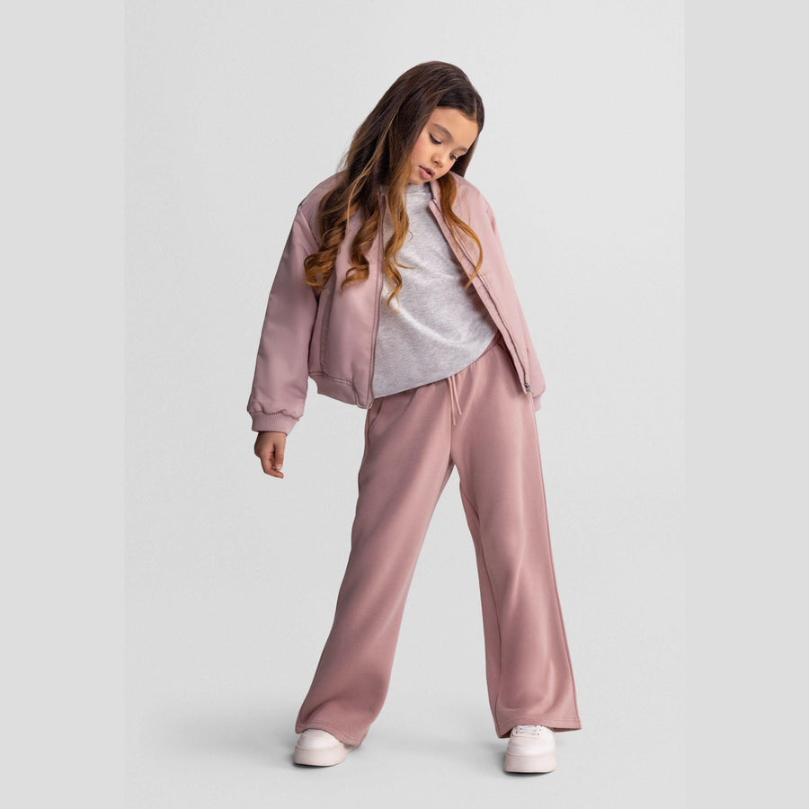 Young woman wearing pink wide leg joggers with grey hoodie and white sneakers against light background, showing relaxed contemporary styling