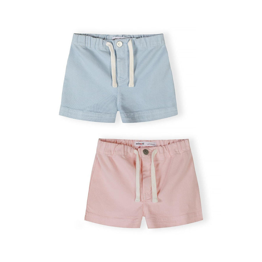 Two pairs of Minoti twill shorts displayed flat - light blue pair on top and soft pink pair below, both featuring white drawstring ties and button fastenings on white background