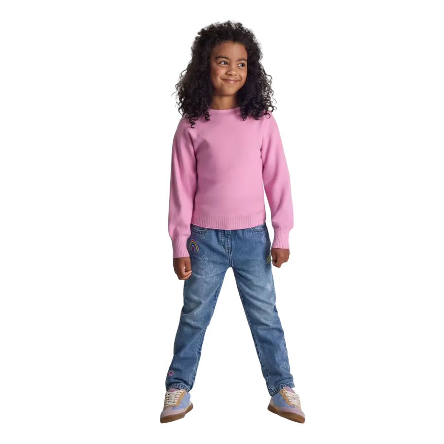 Young girl wearing pink textured knit jumper with boat neckline and blue jeans, full body view on black background