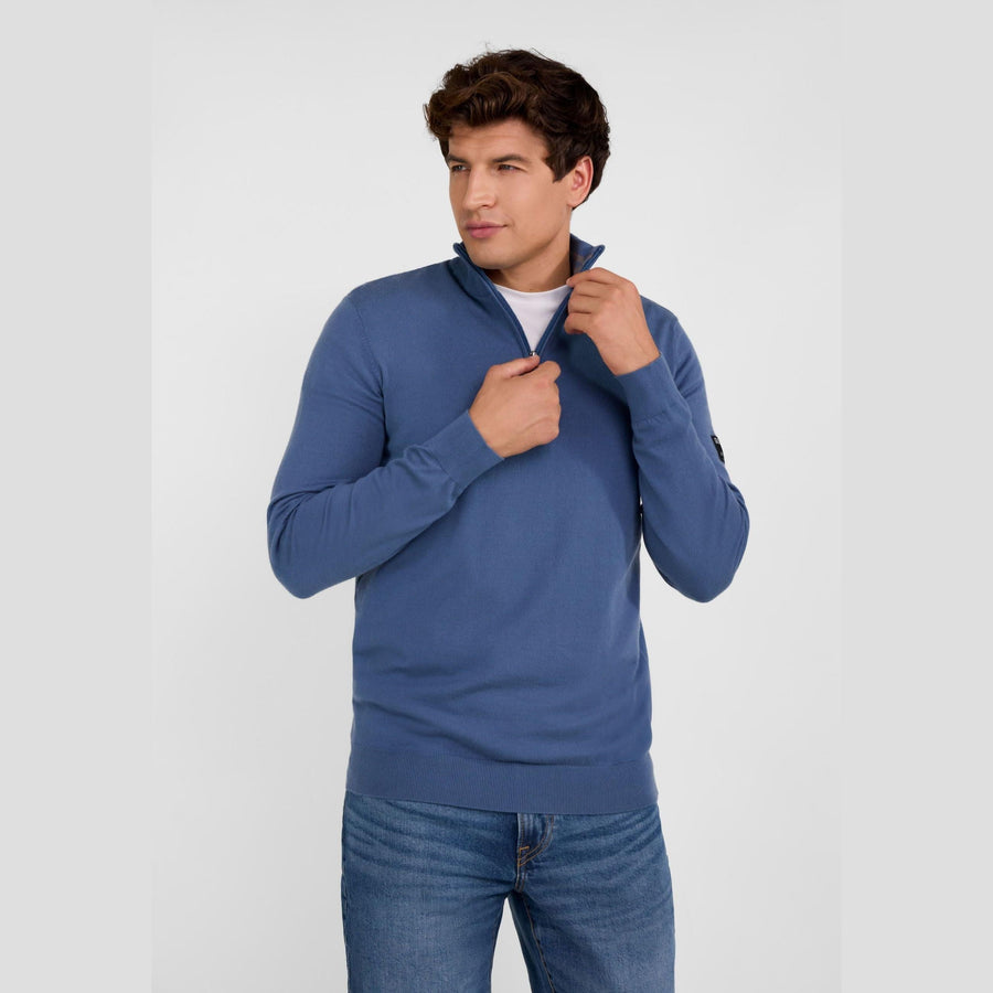 Man wearing blue half zip jumper with stand collar, front view against white background, hands adjusting collar